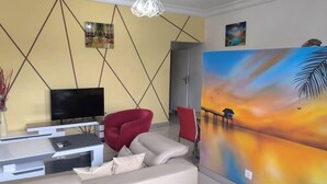 A living room with a TV, red chair, beige sofa, and a large painting on the wall. - Résidence Gian (Libreville)