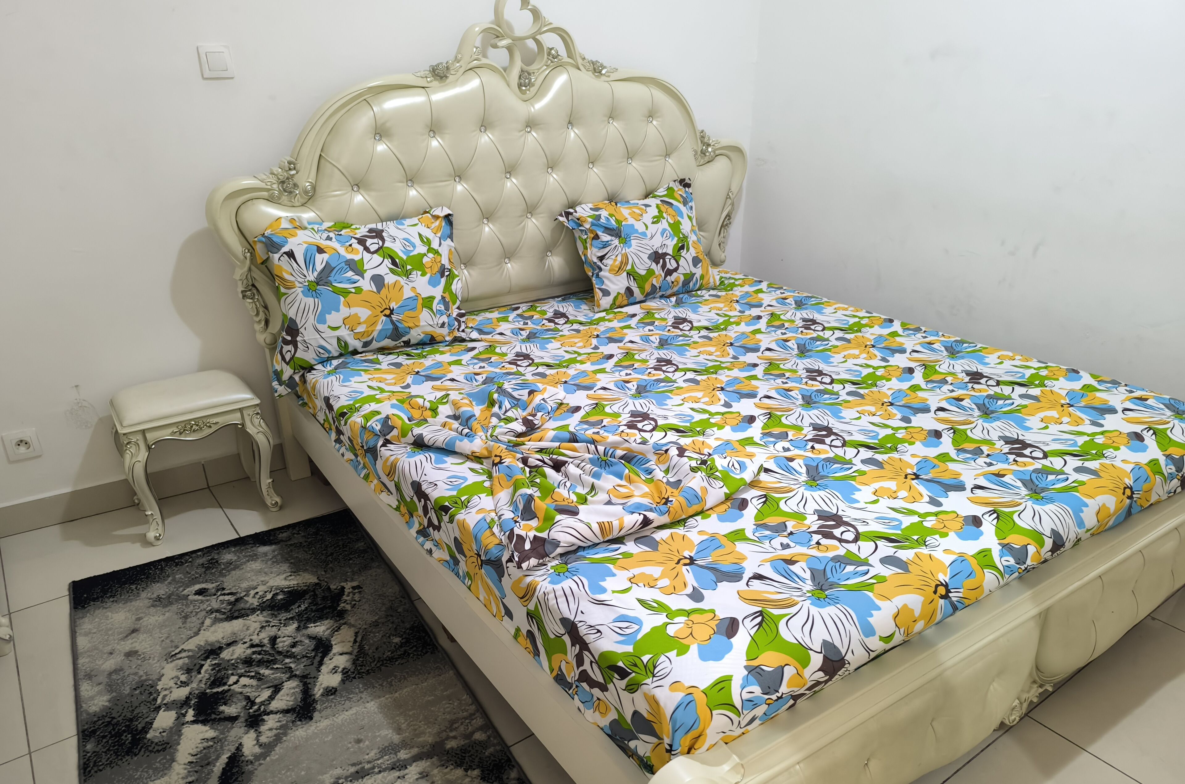 Un letto con copriletto floreale, testiera trapuntata e due cuscini coordinati.