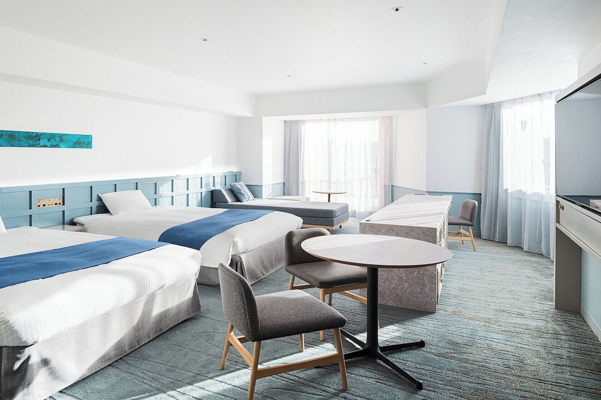 A hotel room with two beds, a desk, a chair, and a TV.