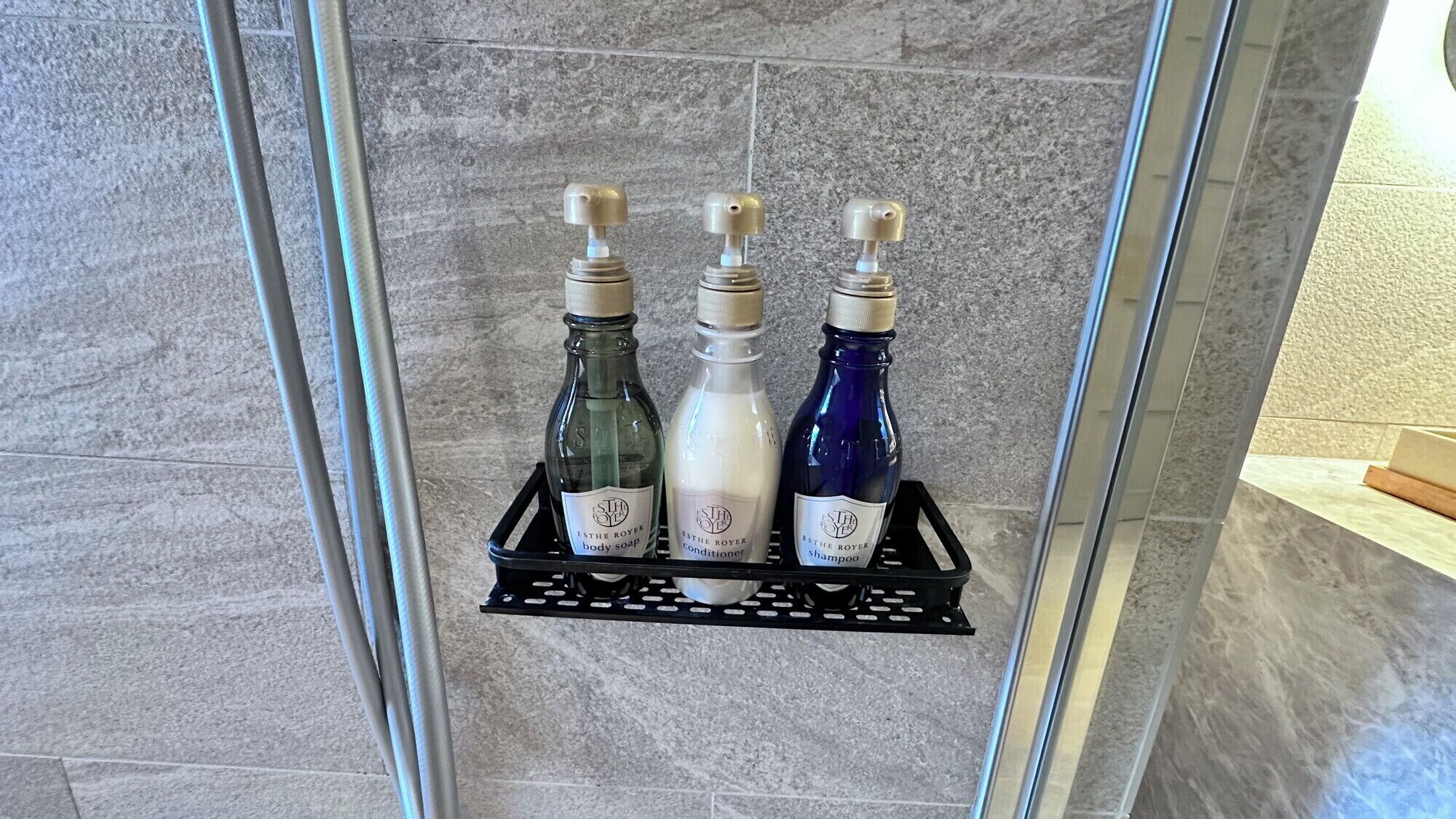 A shower area with a black metal shelf holding three bottles of toiletries.