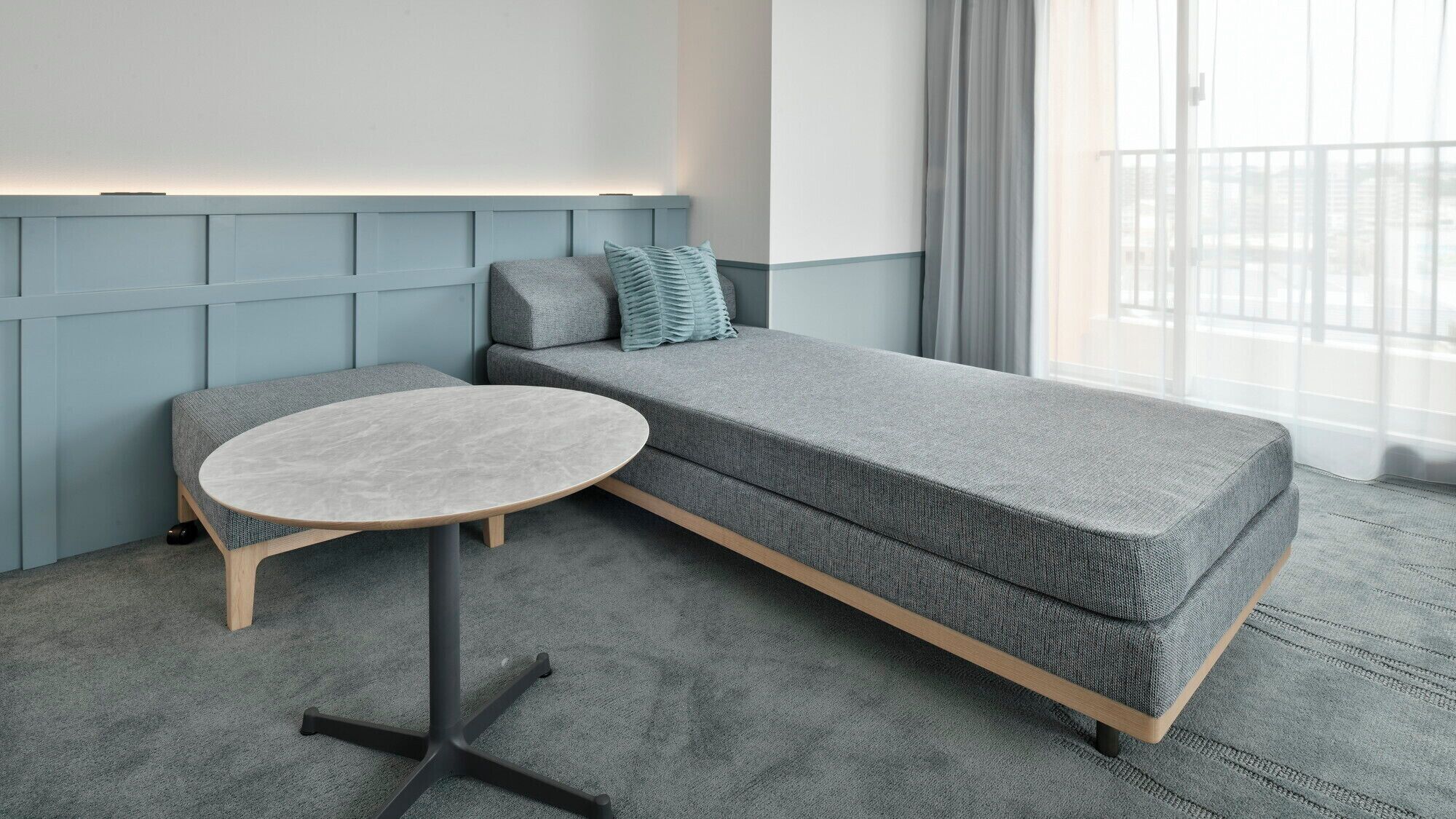 A modern room with a grey sofa, a round table, and a light blue wall panel.