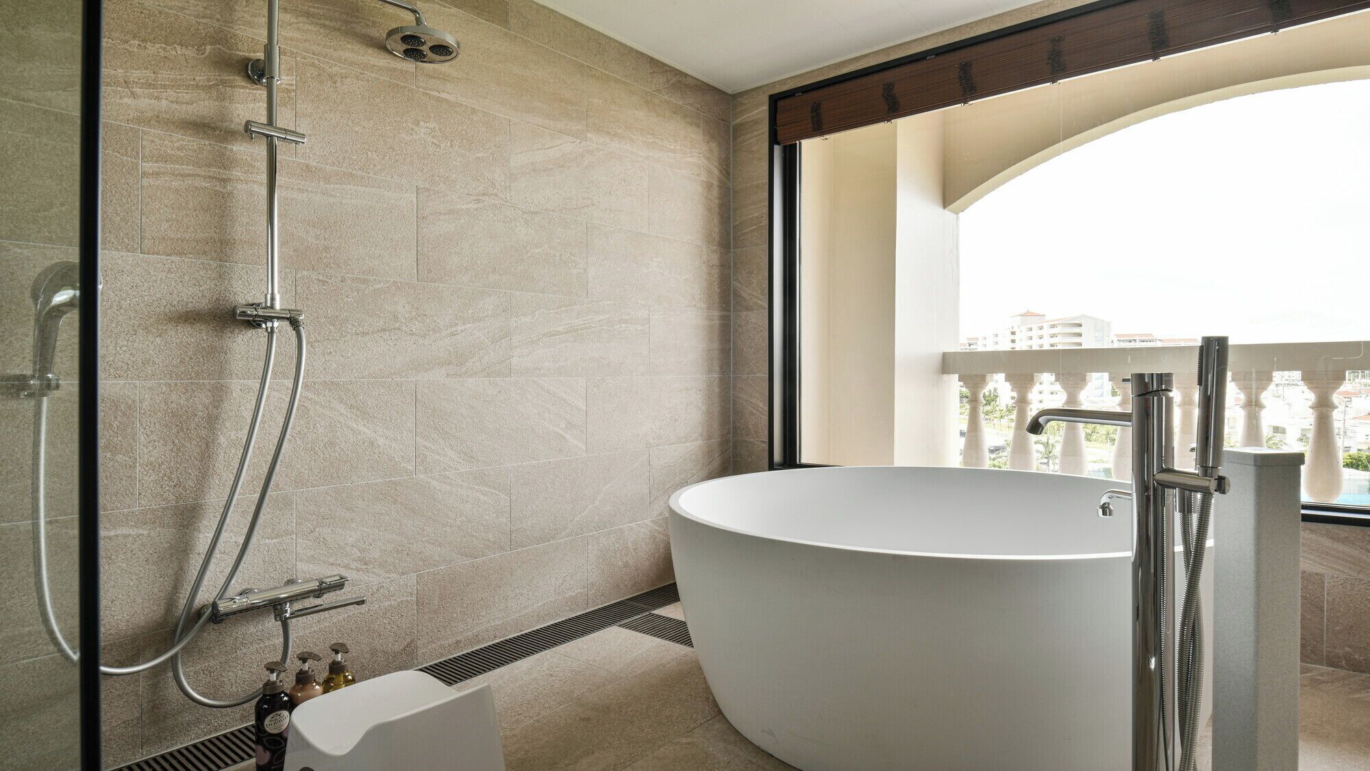 Un baño moderno con una bañera independiente, ducha con cabezal de ducha manual y ventana con vista a un balcón con barandilla.