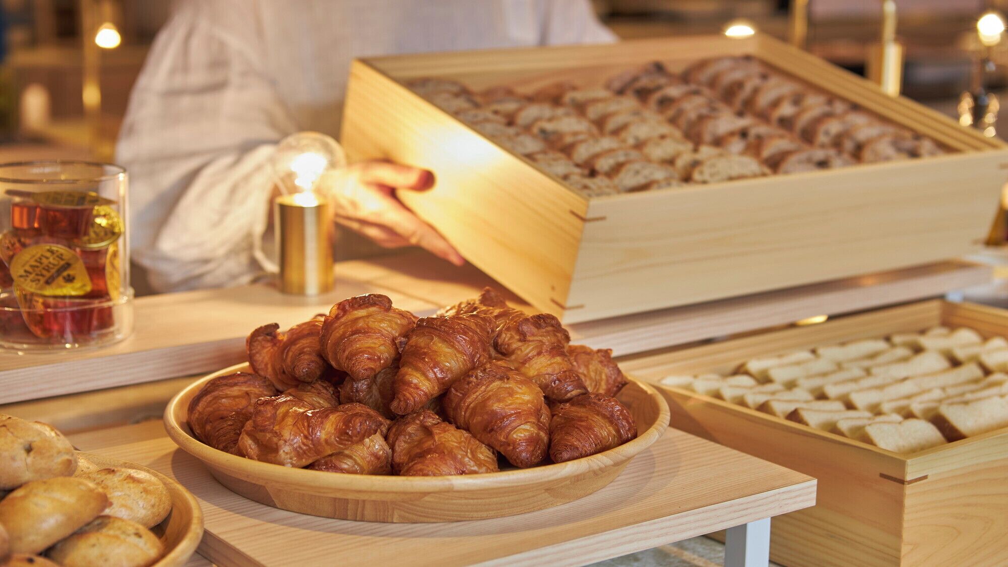 A wooden serving tray with pastries, a wooden box with more pastries, and a glass of a beverage.