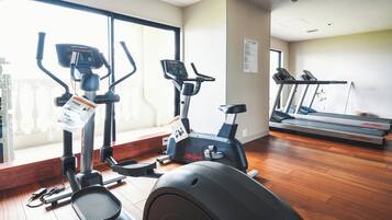 A gym with cardio equipment including treadmills and stationary bikes, wooden flooring, and large windows.