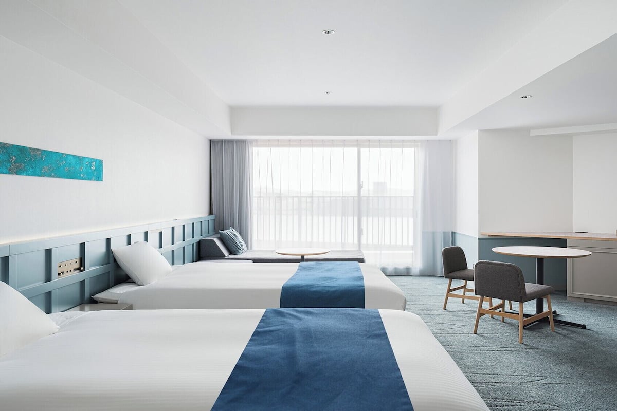 A hotel room with two beds, a desk, and a chair.