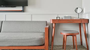 Una habitación moderna con un sofá gris, un escritorio de madera con una silla, un espejo redondo y un reloj.