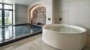 Un área de piscina interior moderna con un amplio jacuzzi circular, una pared de ladrillo y vistas al exterior.