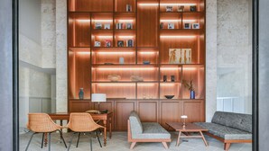 Una sala moderna con una estantería de madera, un comedor con sillas de mimbre y un sofá gris.