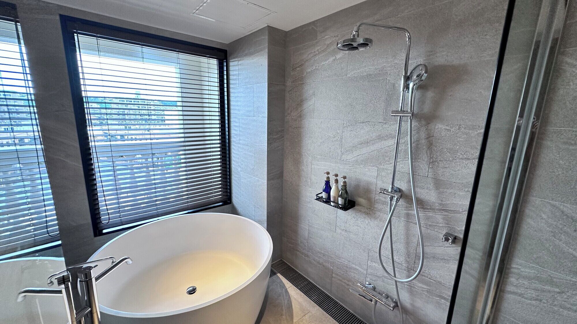 Une salle de bain moderne avec une baignoire sur pieds, une douche à l’italienne et une fenêtre équipée de stores.