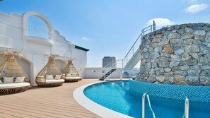 A pool area with a stone wall, lounge chairs, and a staircase leading to an upper deck. - Lequ Okinawa Chatan Spa & Resort (Chatan)