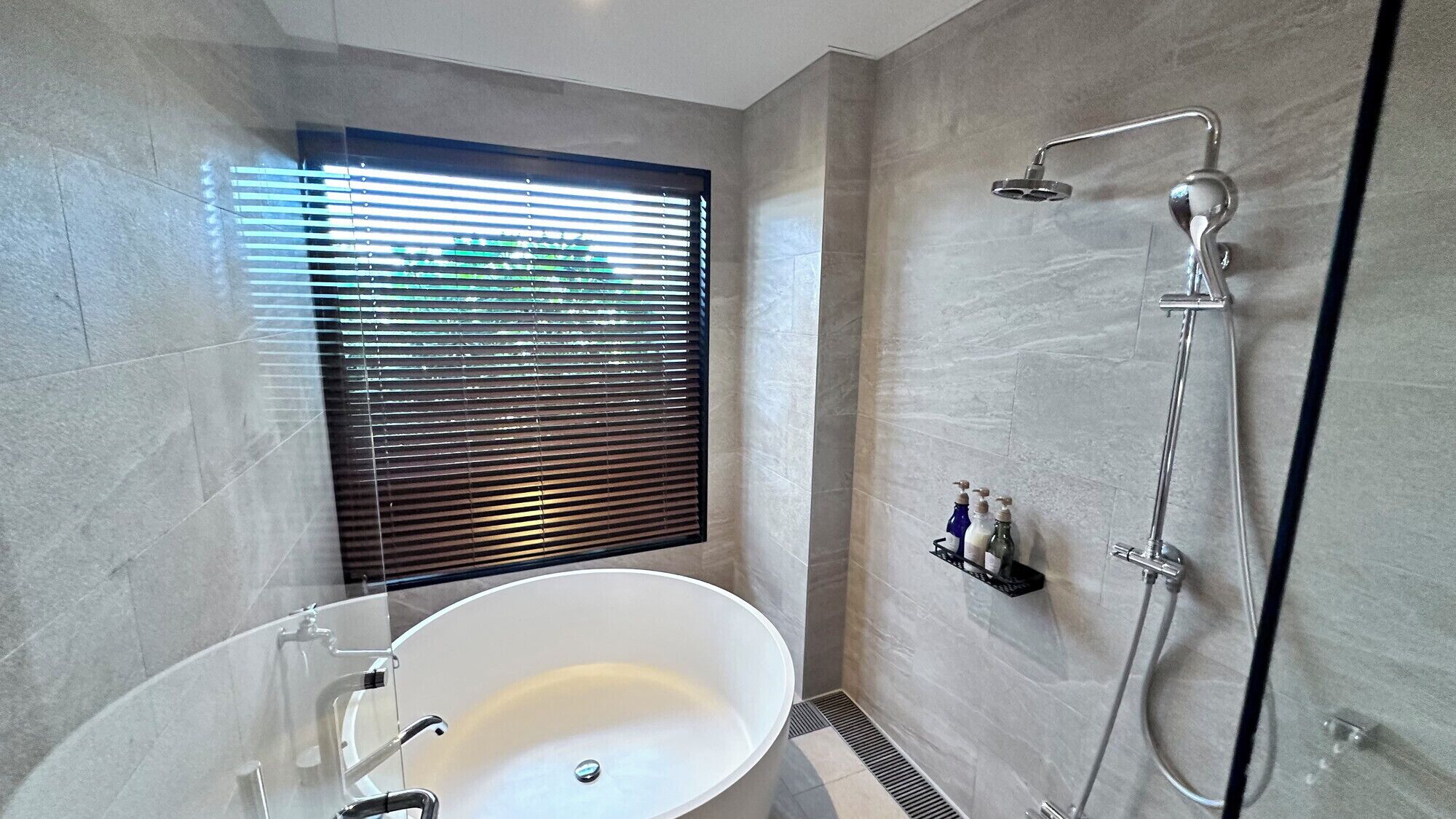 Een moderne badkamer met een vrijstaand bad, een douche met handdouche en een raam met zonwering.
