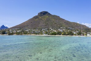 A coastal town with a prominent mountain, clear turquoise waters, and residential buildings along the shore.