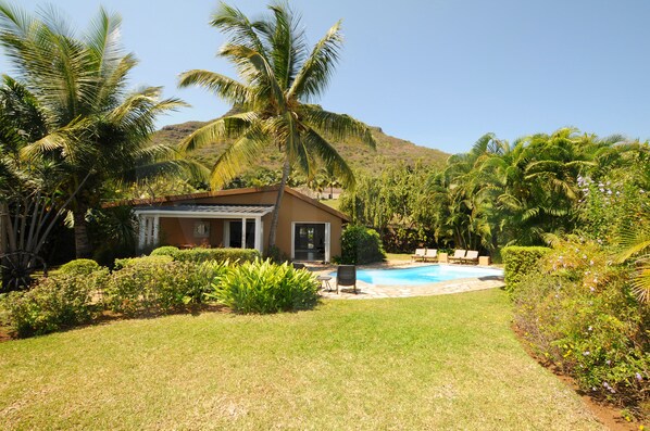 A house with a pool, surrounded by palm trees and a hilly landscape.