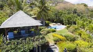 A resort with a pool, lounge chairs, and a covered seating area surrounded by lush greenery and palm trees. - Villa Acassia with 2 rooms (Black River)