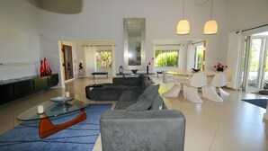 A modern living room with a glass coffee table, grey sofas, and a large mirror. - Villa Acassia with 2 rooms (Black River)