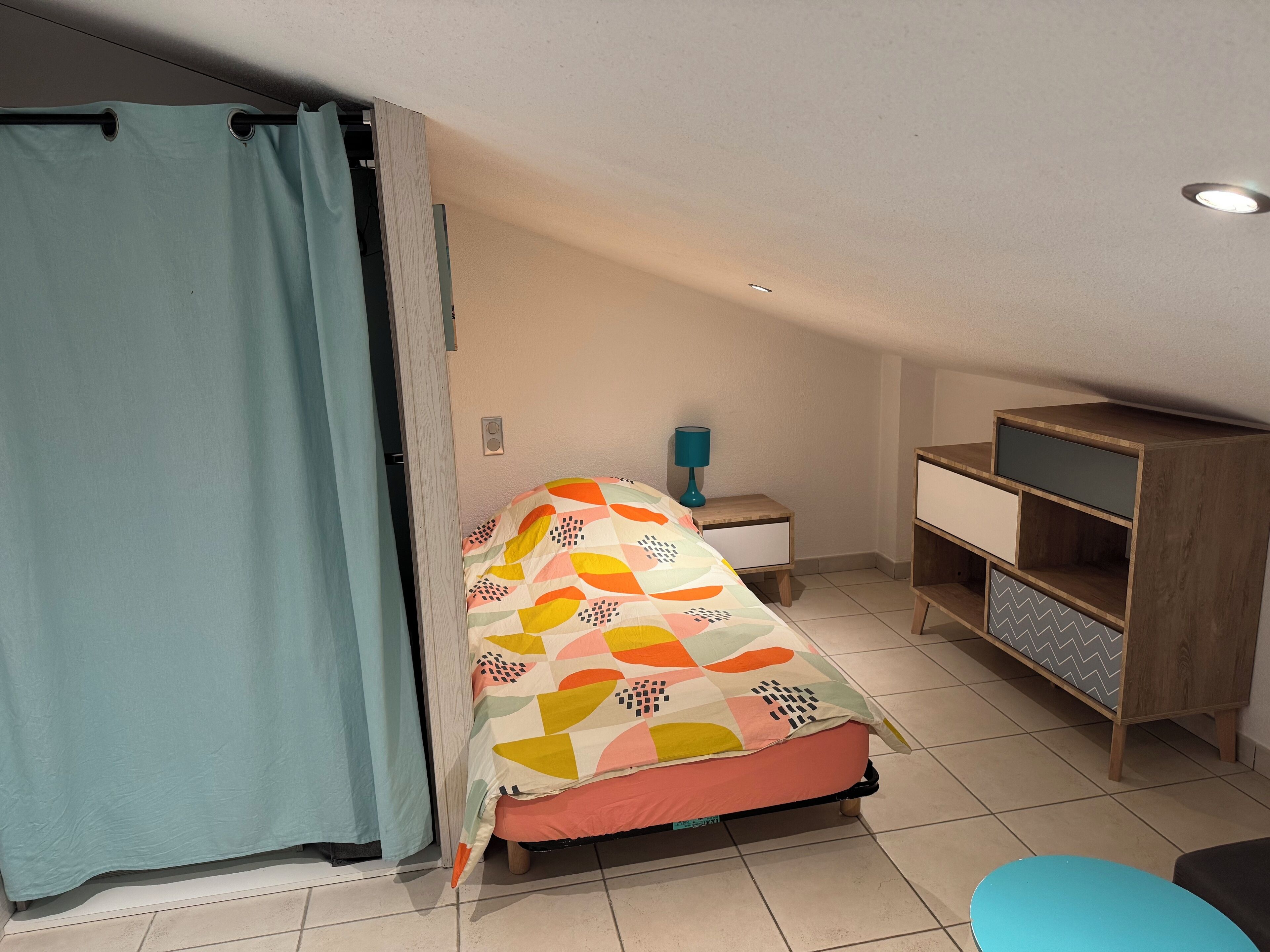 Een slaapkamer met een bed, een nachtkastje, een dressoir en een teal-kleurige stoel.