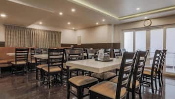 Comedor de hotel con varias mesas y sillas, un reloj en la pared y vistas al exterior a través de grandes ventanales.