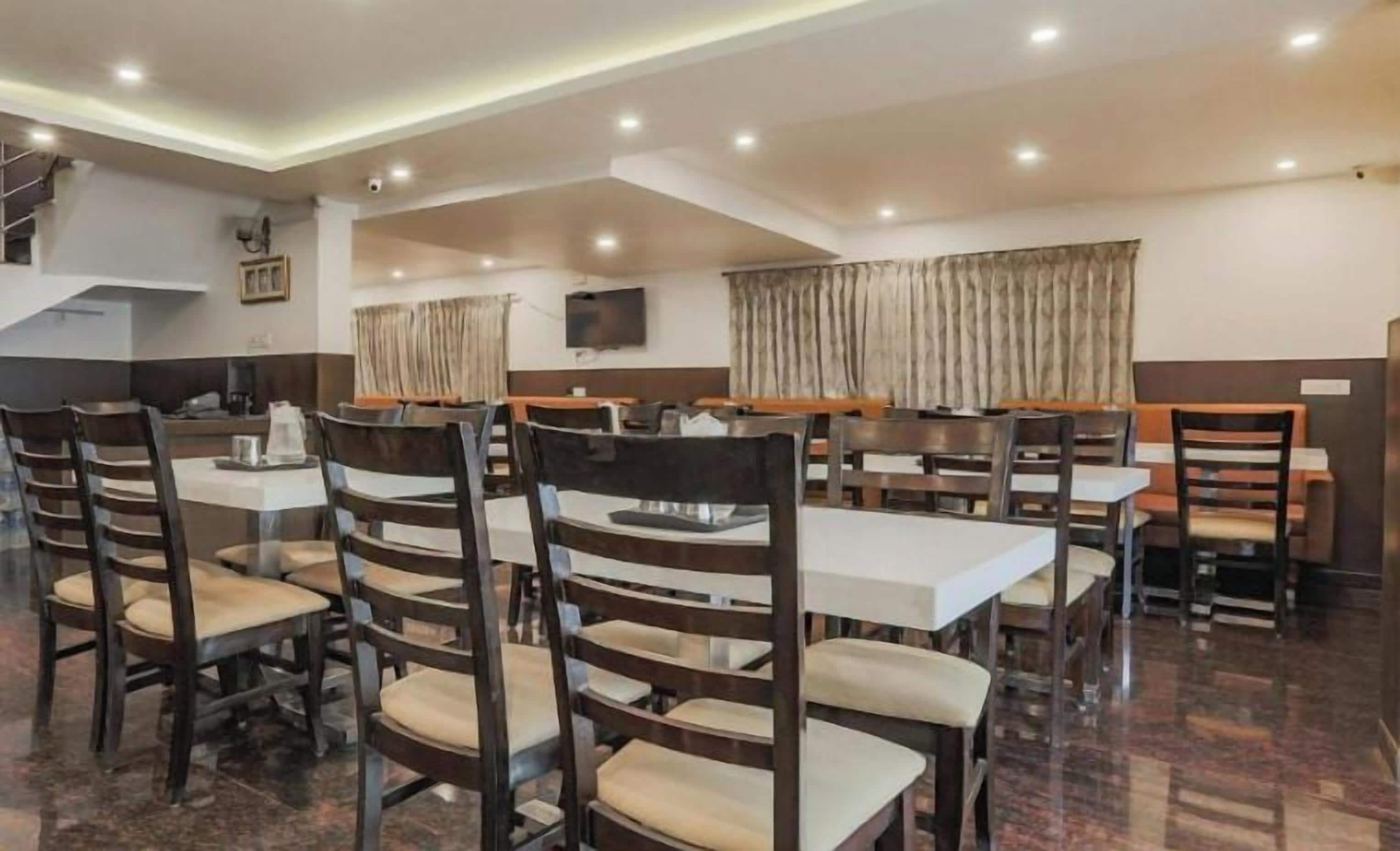 A dining area with multiple tables and chairs, a staircase, and a television on the wall.