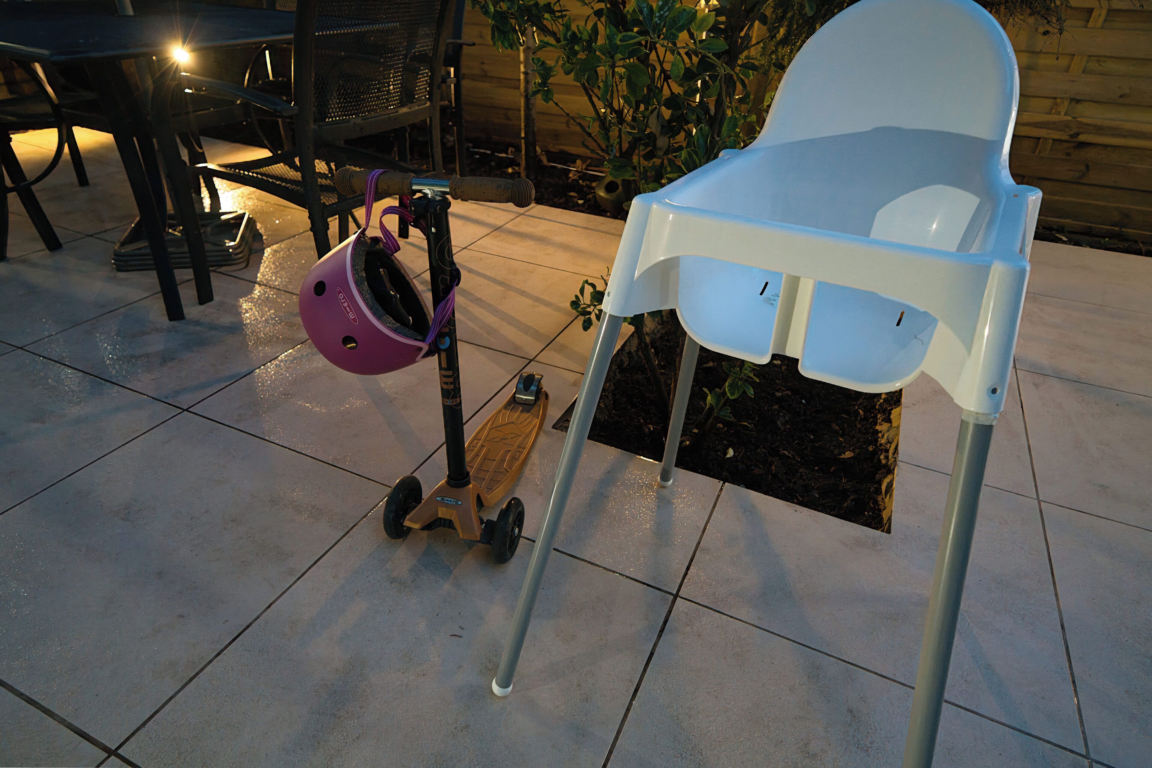 Eine Terrasse mit einem weißen Hochstuhl, einem lila Helm und einem Roller.