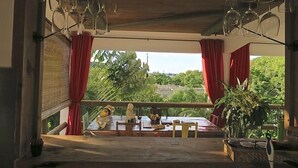 A dining area with a table set for two, a potted plant, and a view of greenery outside.