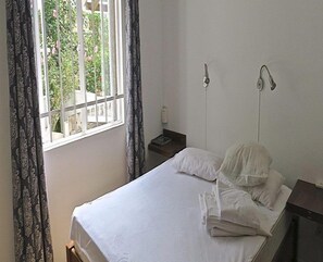 A simple, clean room with a bed, a nightstand, and a window with curtains. - Villa de la Valle (Rodrigues Island)