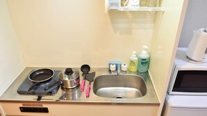 Una kitchenette con estufa, sartén, olla, espátula y pileta. Hay botellas de detergente para platos y una cafetera.