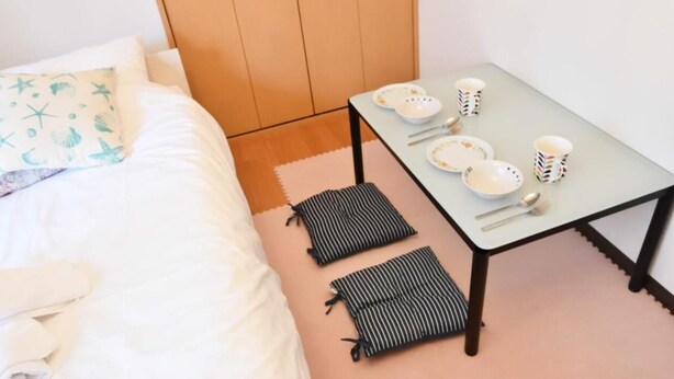 Una cama bien hecha con un cojín estampado con estrellas, una mesita con platos y tazas, y cojines a rayas.