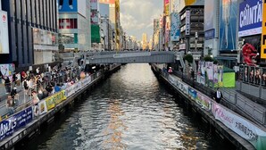 Una concurrida calle urbana con un canal, flanqueada por edificios comerciales y anuncios.
