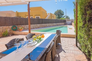 An outdoor pool area with a dining table set for four, surrounded by wicker chairs.