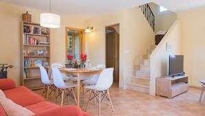 A living room with a red sofa, a dining table with chairs, a bookshelf, a TV on a stand, and a staircase. - Villa Sebastian in Sa Rapita, close from the sea. (Sa Ràpita)