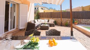 An outdoor patio with a dining table set for two, wicker furniture, and a stone wall backdrop. - Villa Sebastian in Sa Rapita, close from the sea. (Sa Ràpita)