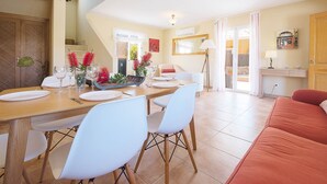 A dining area with a wooden table set for four, white chairs, and a red sofa in the foreground. - Villa Sebastian in Sa Rapita, close from the sea. (Sa Ràpita)