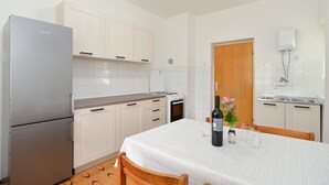 A compact kitchen with white cabinets, a built-in oven, a refrigerator, and a dining area with a table set for two. - Apartment 407/923 (Istria - Fažana), 750m from the beach (Fažana)