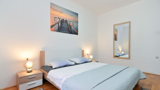 A bedroom with a bed, bedside tables, a nightstand, a wall-mounted mirror, and a painting of a pier. - Apartment 407/923 (Istria - Fažana), 750m from the beach (Fažana)