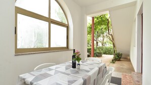 A dining area with a table set for two, a large arched window, and a view of a garden. - Apartment 407/923 (Istria - Fažana), 750m from the beach (Fažana)