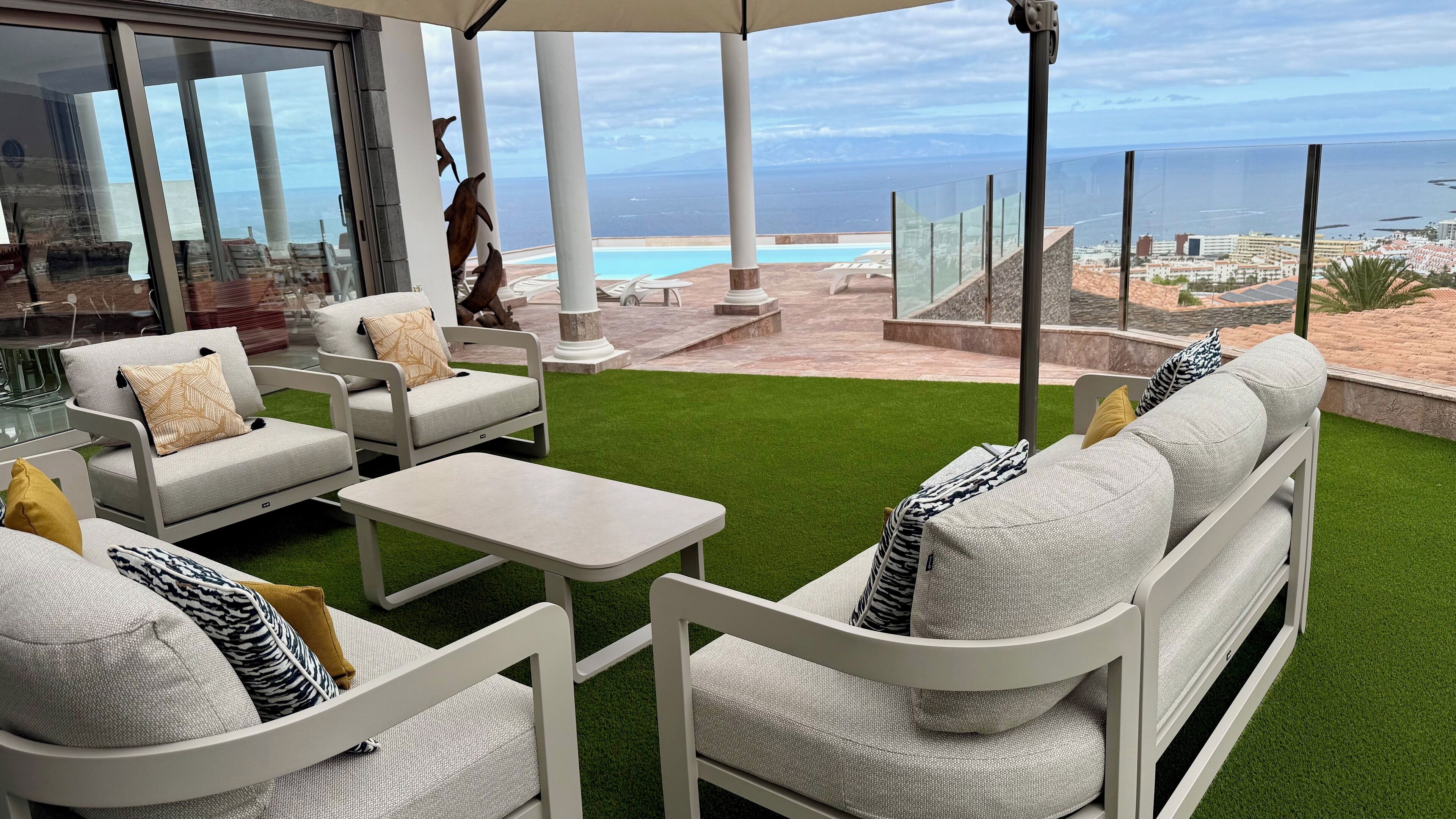 A patio with white furniture, a small table, and a view of the ocean and cityscape.