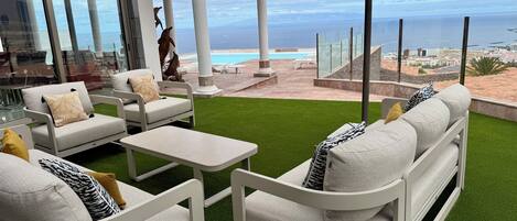 A patio with white furniture, a small table, and a view of the ocean and cityscape.