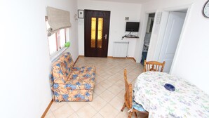 Una habitación con sofá, una mesa de comedor con sillas, televisor y una puerta con ventanal.