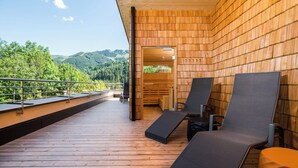 Een houten terras met lounge fauteuils en uitzicht op een bebost berglandschap.