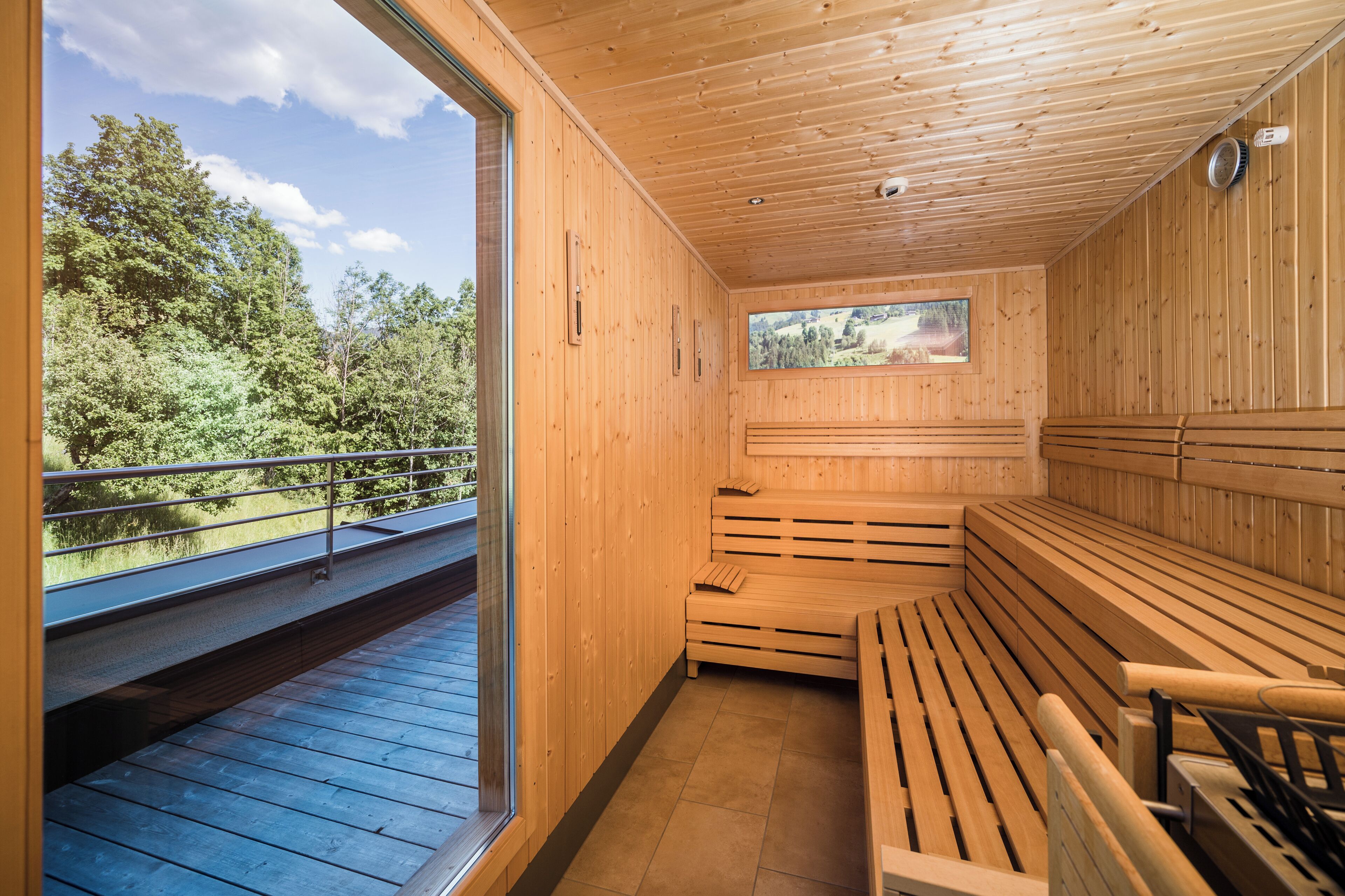 A wooden sauna with benches and a window overlooking a forested area.