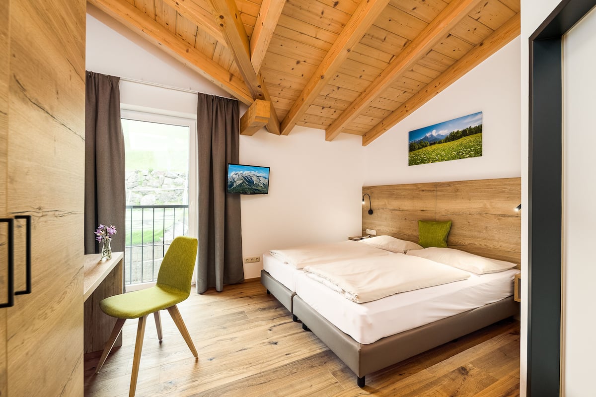 Un dormitorio con techo de madera, una cama, un escritorio con silla y una ventana con cortinas.