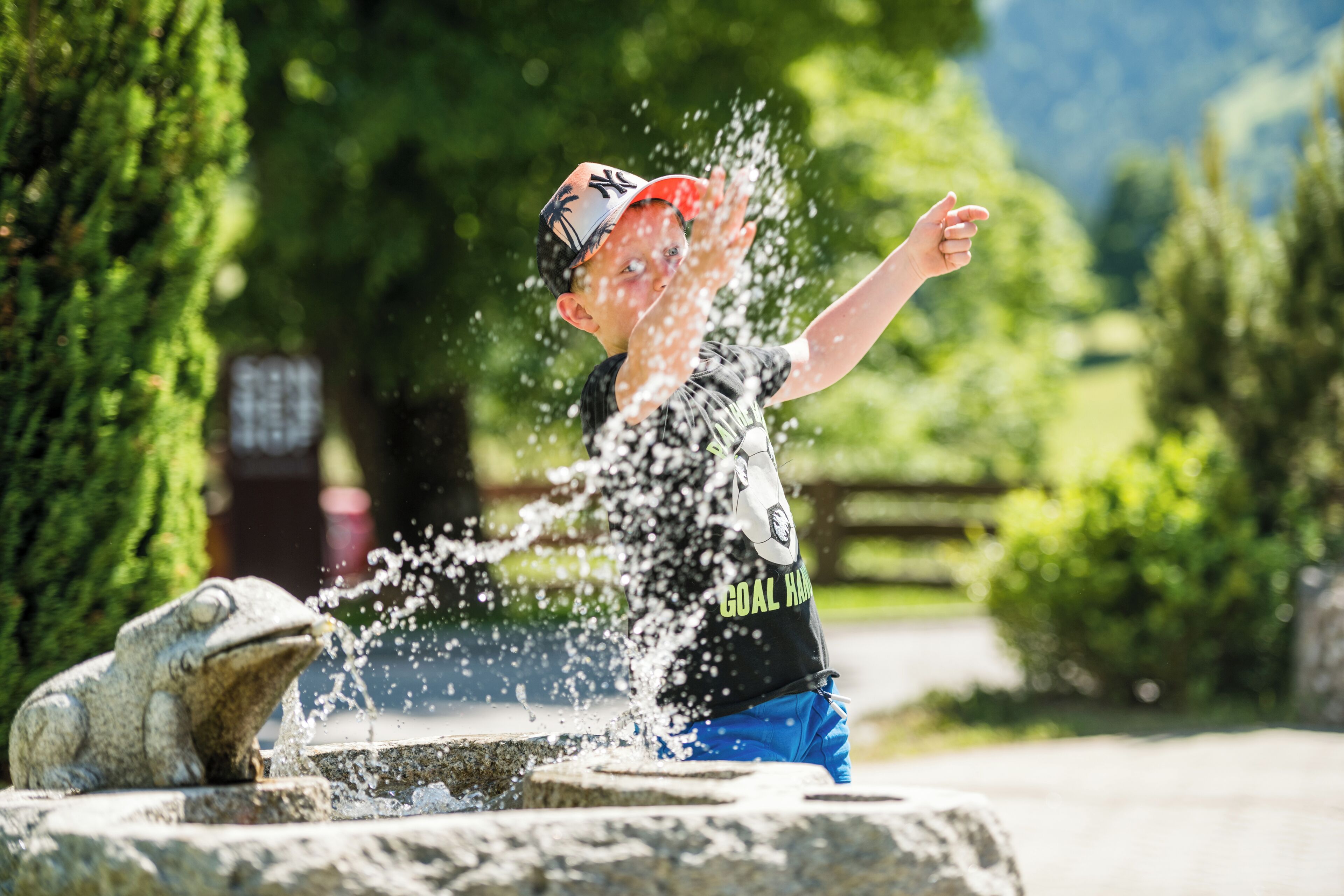 A child playing with water at a fountain in a park.