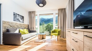 Een moderne woonkamer met een bank, salontafel en televisie, een accentmuur van steen, houten vloeren en uitzicht op bergen.