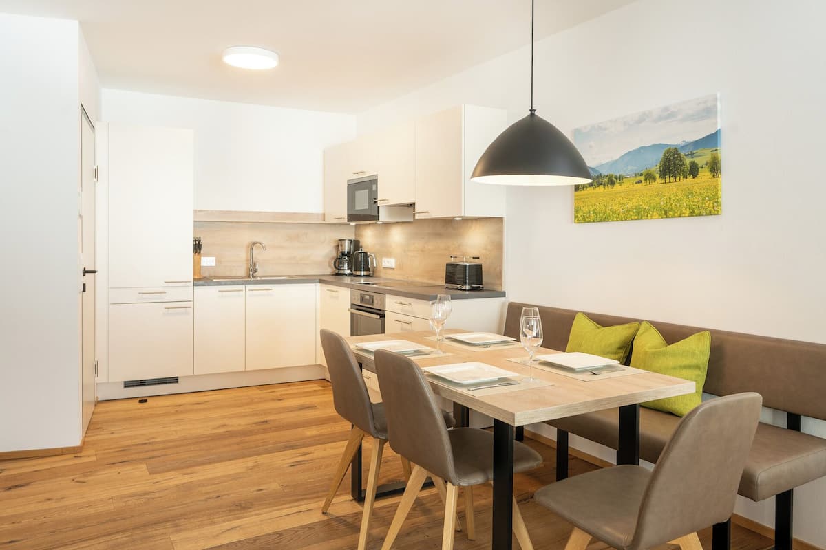 Una cocina moderna con armarios blancos, una mesa de comedor con cuatro sillas y una lámpara colgante negra.