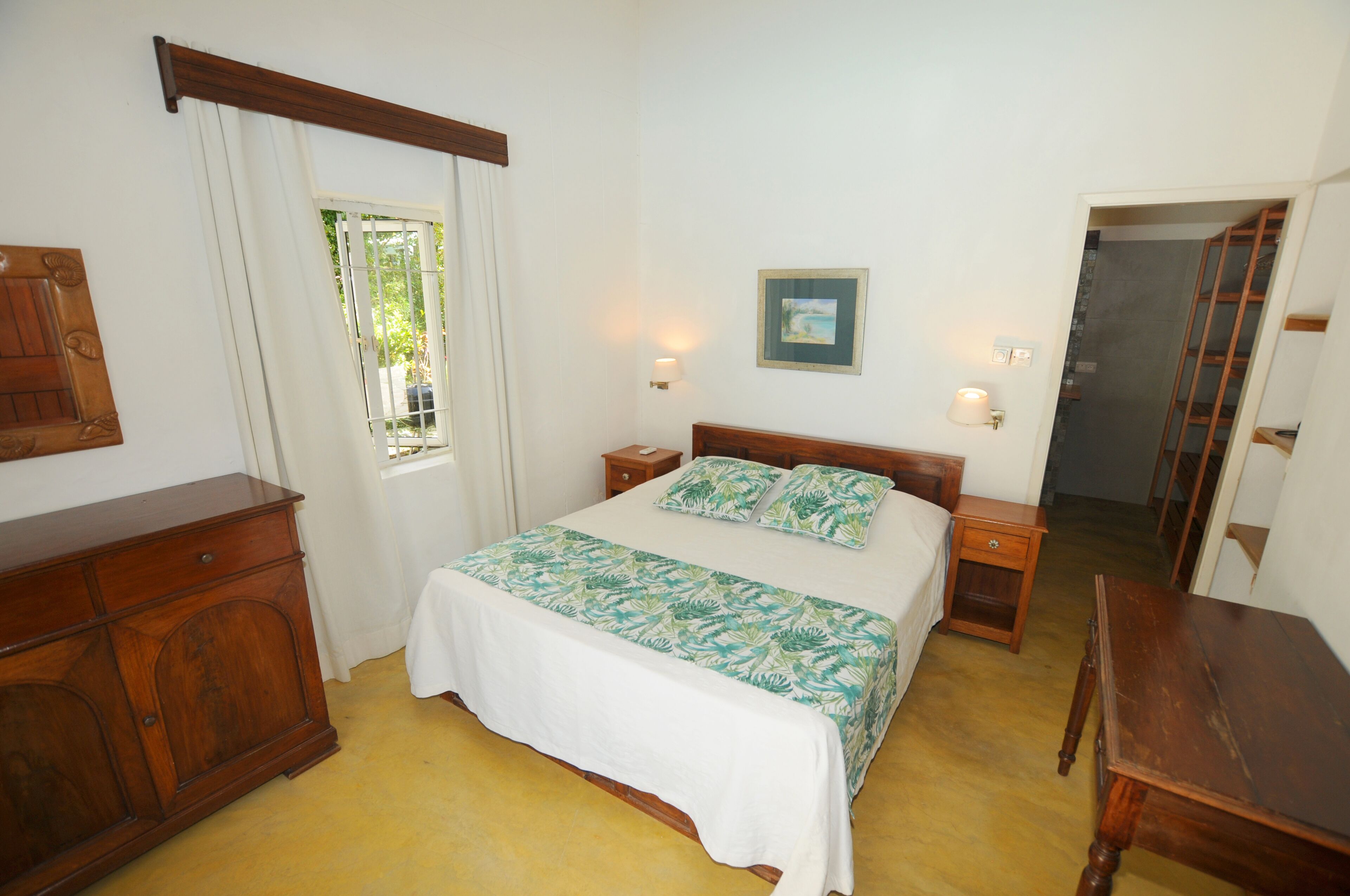 A bedroom with a bed, nightstands, a wooden dresser, a window with curtains, and a framed picture on the wall.