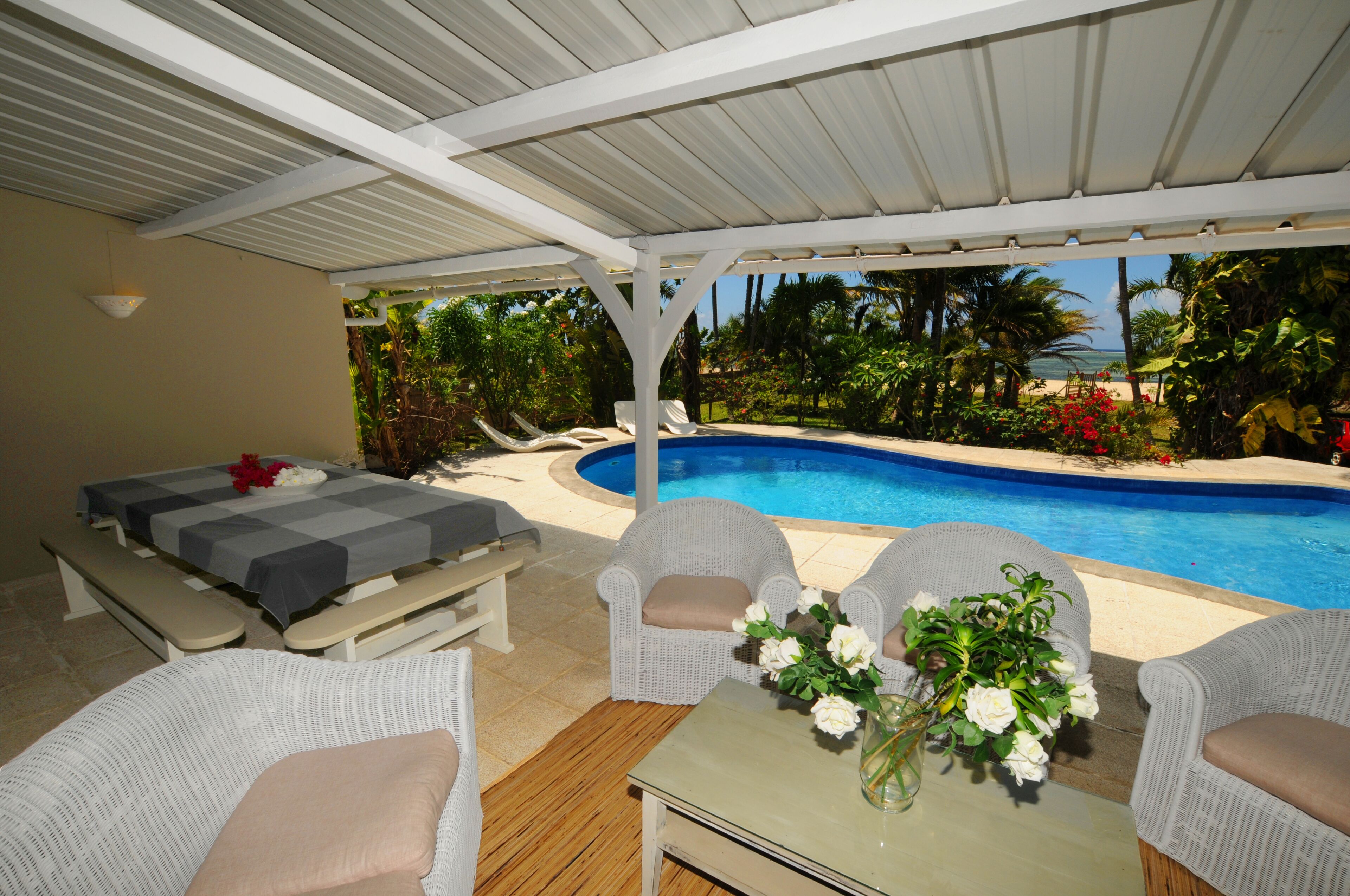 Un espacio al aire libre techado con piscina, sillas de descanso y una mesa con flores.