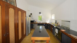A kitchen with a long wooden table, a stove, and a refrigerator. - Villa Philibert (Surinam)