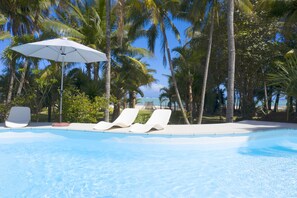 A pool with lounge chairs and an umbrella, surrounded by palm trees and a clear sky. - Villa Philibert (Surinam)
