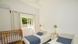 A bedroom with two beds, a wooden crib, a window with curtains, and a ceiling fan. - Villa Philibert (Surinam)