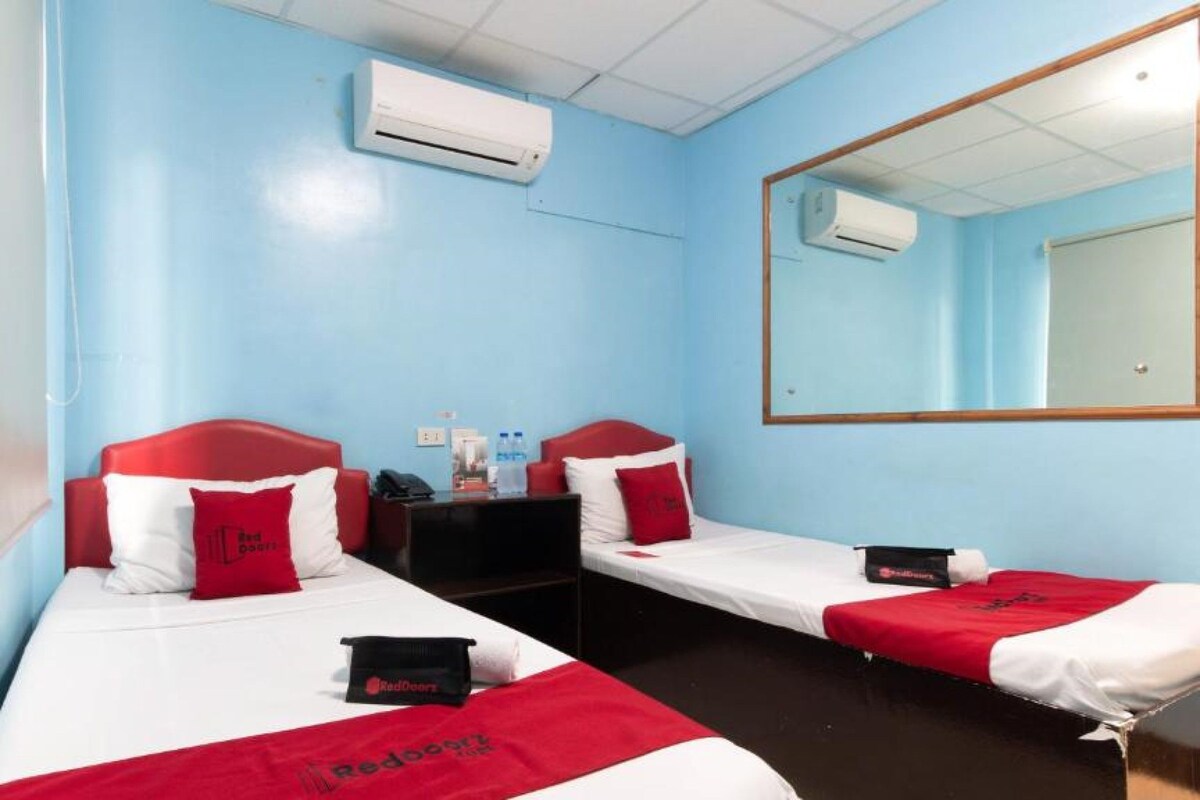 Habitación de hotel con dos camas individuales, un escritorio, una silla, un espejo y un equipo de aire acondicionado.